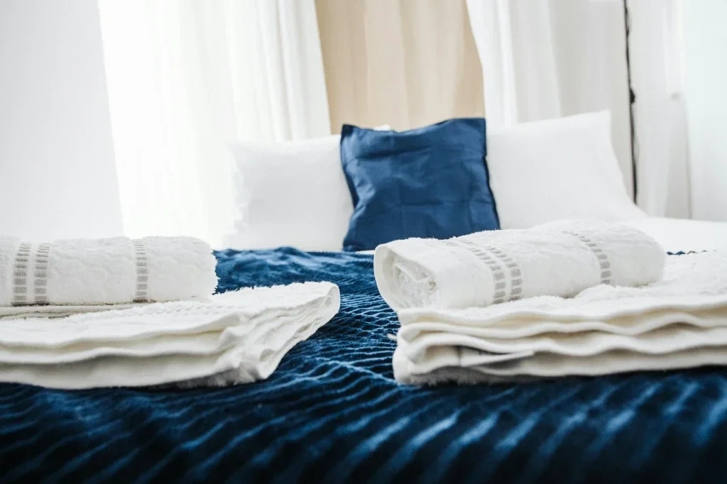 Pristine Airbnb turnover cleaning setup featuring a neatly made bed with rolled white towels in a sunlit room, showcasing Splash Maids' hotel-standard hospitality.